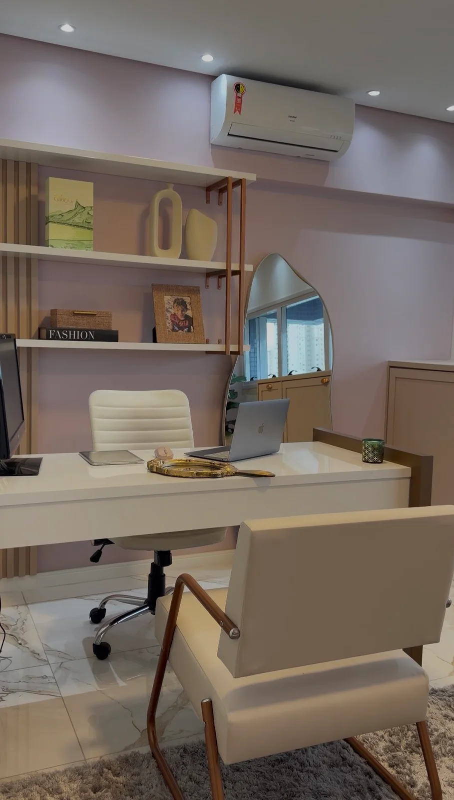 Mesa clara com duas poltronas, estante e espelho de contorno orgânico